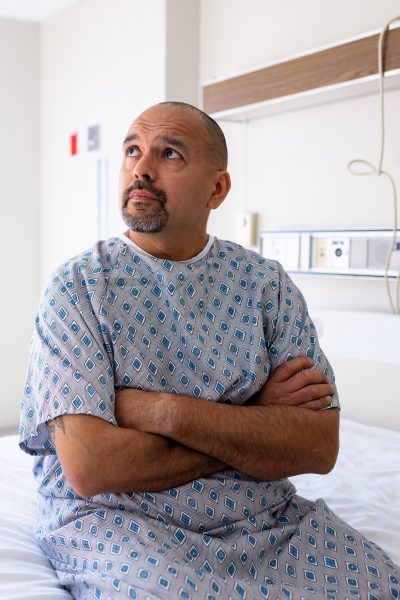 Mature hispanic male patient in a hospital gown waiting on the bed